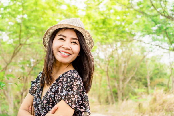 beautiful asian woman wearing a hat and smiling outdoors in green park